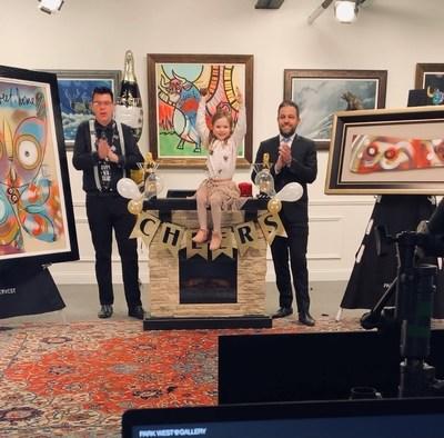 Park West Gallery Senior Auctioneer Jordan Sitter and host David Gorman celebrate with Jasmyne Sitter, a 4-year-old art-training auctioneer.